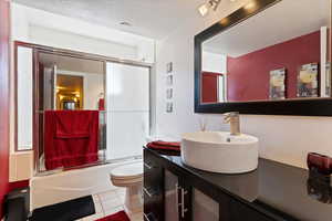 Bathroom featuring vanity, a textured ceiling, bath / shower combo with glass door, and light tile patterned floors