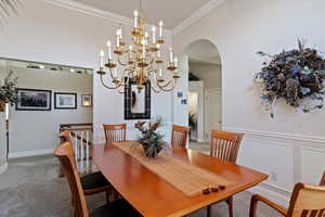 Carpeted dining room with arched walkways, ornamental molding, hanging lights, and a high ceiling
