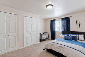 Bedroom with two closets, carpet, and a textured ceiling