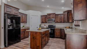 Kitchen with black appliances, dark wood finish cabinets, a center island, lofted ceiling, and light stone countertops.