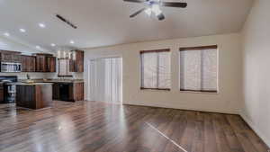 Kitchen with a center island, vaulted ceiling, dark wood finish cabinets, stainless steel appliances, and hanging light fixtures