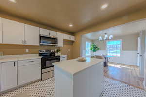 Kitchen featuring wainscoting, stainless steel appliances, white cabinetry, a center island, and updated countertops