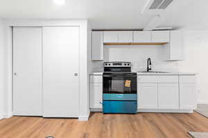 Kitchen featuring electric range, white cabinets, and light wood-style floors