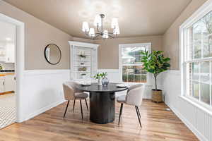 Dining space featuring light wood-style flooring, wainscoting, suspended lighting, and a textured ceiling