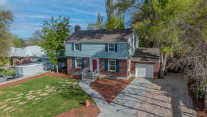 Colonial house with concrete driveway, a chimney, an attached garage, brick siding, and a front yard