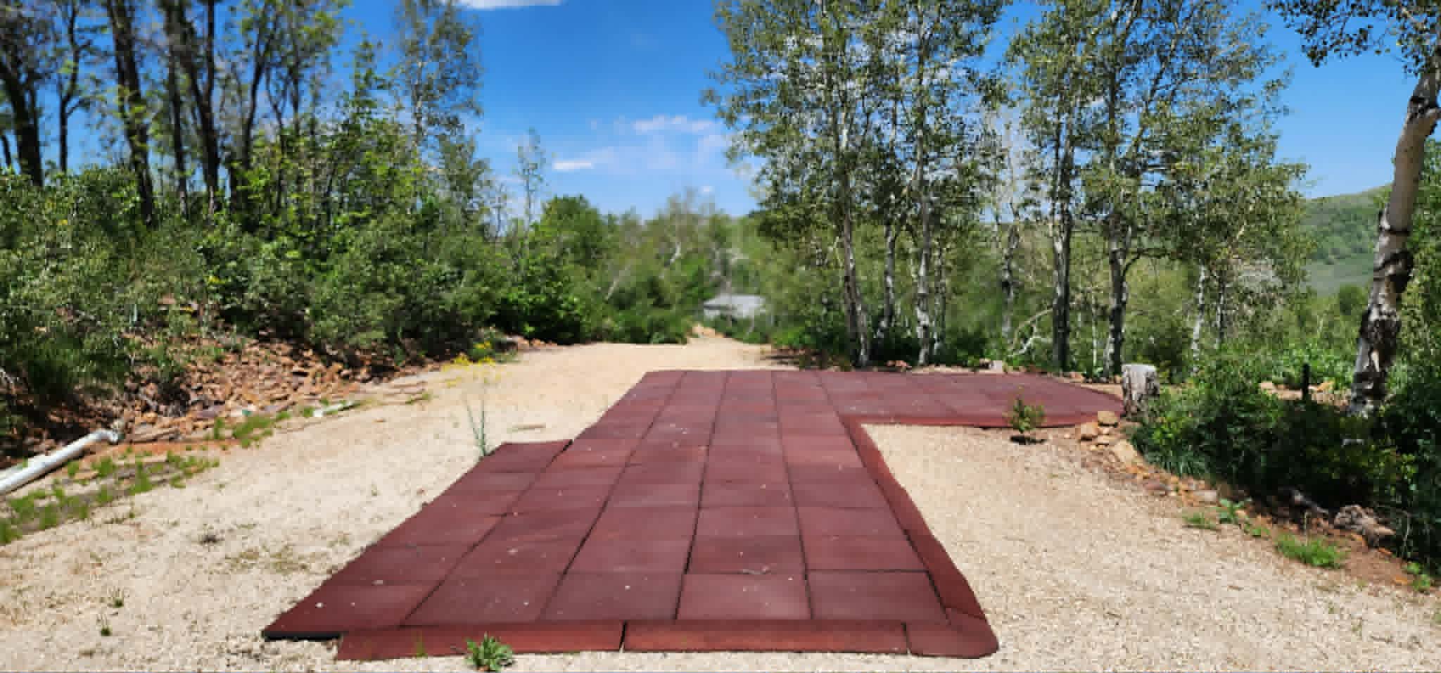 Outdoor area featuring red modular surfacing, gravel ground cover, and surrounding mature trees