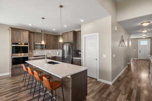 Kitchen featuring stainless steel appliances, a breakfast bar area, an island with sink, light stone countertops, and dark wood-style flooring