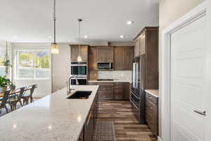 Kitchen with dark wood-style floors, stainless steel appliances, light stone countertops, pendant lighting, and decorative backsplash