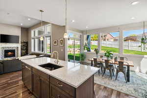 Kitchen featuring dark wood finish cabinetry, open floor plan, light stone counters, a tiled fireplace, and dark wood-style floors