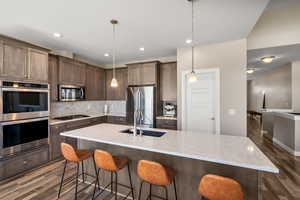 Kitchen with stainless steel appliances, light stone counters, backsplash, pendant lighting, and dark wood-style floors