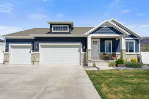 View of front facade featuring stone siding, an attached garage, a front yard, covered porch, and driveway