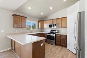 Kitchen featuring stainless steel appliances, a peninsula, vaulted ceiling, light wood finished floors, and recessed lighting