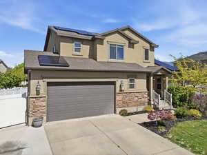 View of front of property with roof mounted solar panels, stone siding, stucco siding, and roof with shingles