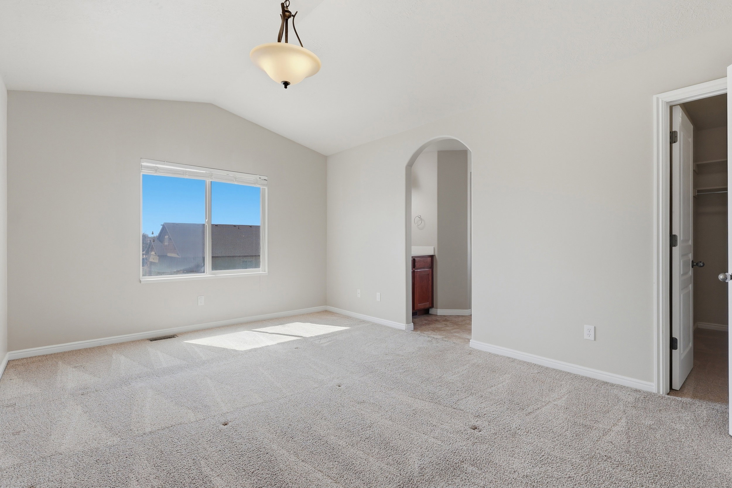 Unfurnished bedroom with a walk in closet, lofted ceiling, light carpet, arched walkways, and connected bathroom