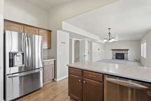 Kitchen with stainless steel appliances, open floor plan, hanging lights, light wood-style flooring, and a stone fireplace