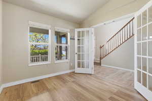 Spare room with french doors, vaulted ceiling, and light wood-style floors