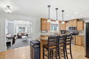Kitchen with backsplash, stainless steel appliances, open floor plan, light wood finished floors, and ornamental molding
