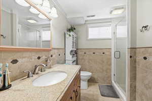 Full bath featuring vanity, a stall shower, wainscoting, healthy amount of natural light, and tile walls