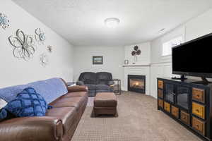 Carpeted living area featuring a glass covered fireplace and a textured ceiling