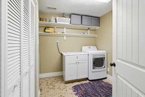 Laundry room featuring a textured ceiling, light tile patterned flooring, and cabinet space
