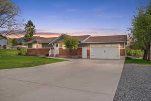 View of front of home with brick siding, a lawn, driveway, an attached garage, and a shingled roof