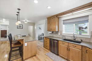Kitchen featuring light stone countertops, a breakfast bar, dishwasher, wood finish cabinetry, and pendant lighting