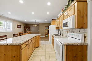 Kitchen with white appliances, stone tile flooring, light stone countertops, a kitchen island, and crown molding