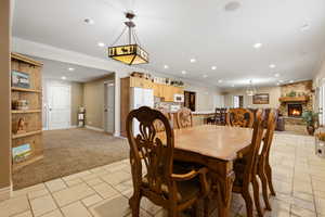 Dining space featuring a fireplace, light carpet, recessed lighting, crown molding, and stone tile flooring