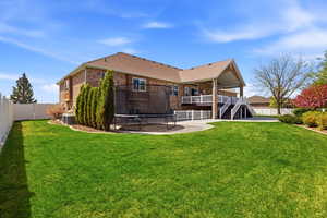 Back of house featuring a trampoline, a fenced backyard, a patio area, brick siding, and a wooden deck