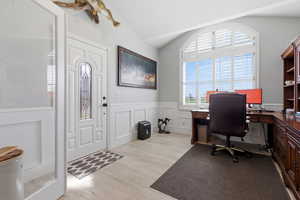 Office area with light wood finished floors, lofted ceiling, a decorative wall, and wainscoting