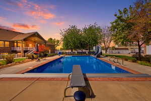Pool at dusk featuring a patio area, a diving board, a water slide, and a fenced backyard