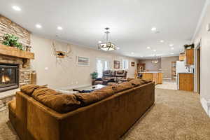 Living area with a stone fireplace, light colored carpet, crown molding, and recessed lighting