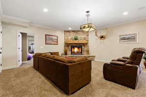 Living area with light colored carpet, a stone fireplace, ornamental molding, and recessed lighting