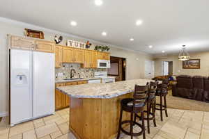 Kitchen featuring white appliances, crown molding, light stone counters, backsplash, and a kitchen bar