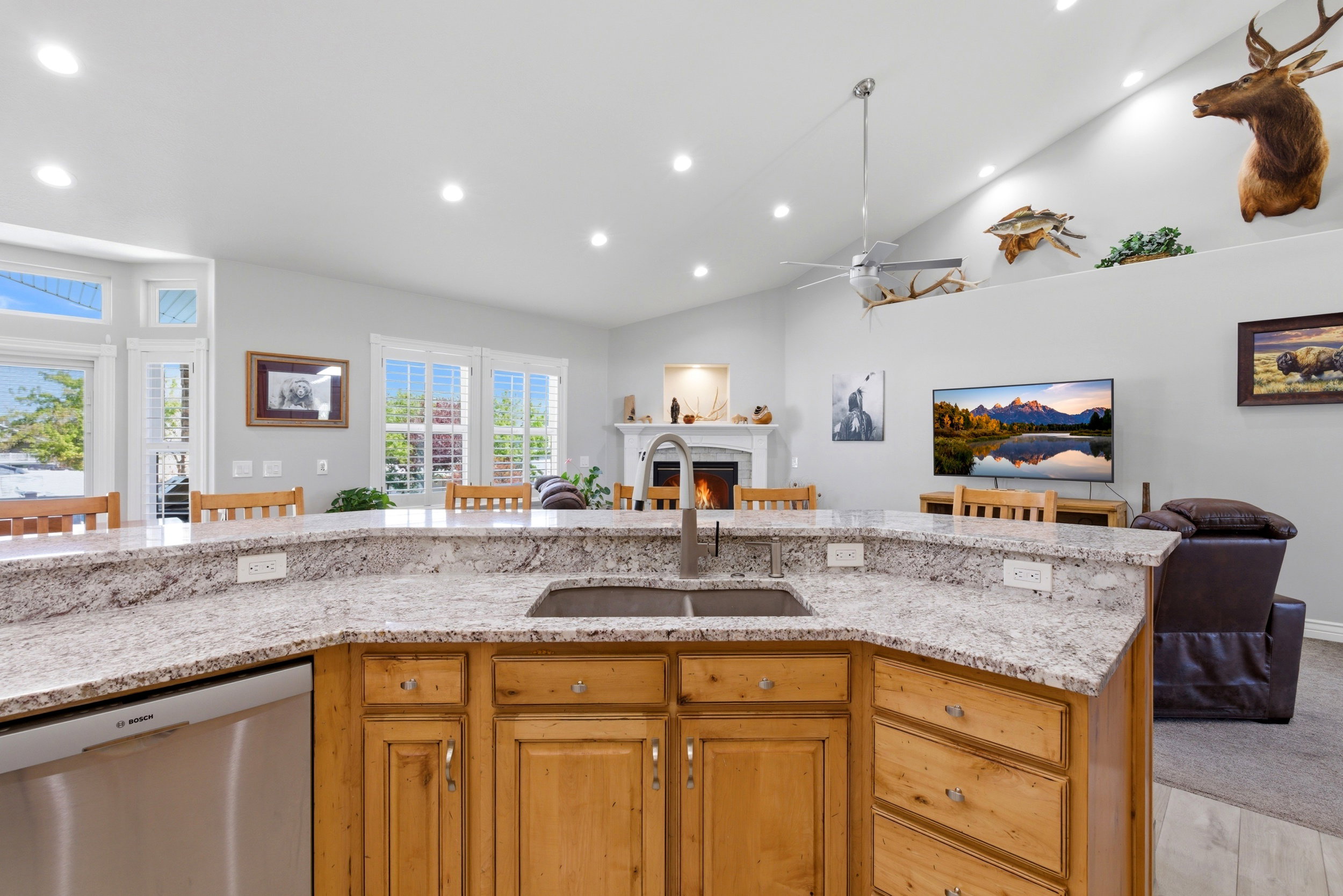 Kitchen with open floor plan, dishwasher, light stone countertops, a lit fireplace, and a ceiling fan