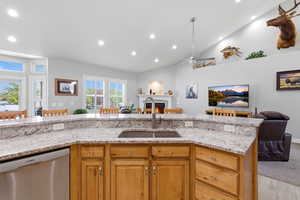 Kitchen with open floor plan, dishwasher, light stone countertops, a lit fireplace, and a ceiling fan