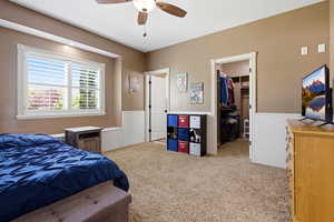 Bedroom with light colored carpet, a spacious closet, and a ceiling fan