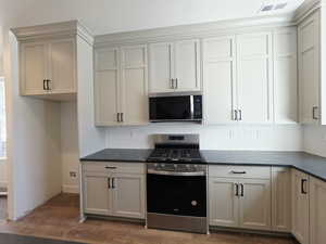 Kitchen featuring stainless steel appliances, decorative backsplash, dark wood-style floors, and dark stone counters