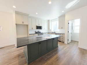 Dual tone kitchen featuring two tone color scheme, dark stone countertops, stainless steel appliances, light wood-style floors, and a kitchen island