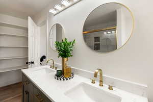 Bathroom with double vanity, dark wood finished floors, and tiled shower