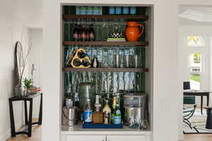 Bar area featuring open shelves, light wood finished floors, white cabinets, and light countertops