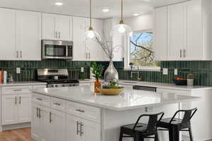 Kitchen with white cabinetry, stainless steel appliances, a breakfast bar, and light stone countertops