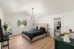 Bedroom with light wood finished floors, a textured ceiling, ensuite bathroom, and hanging lights