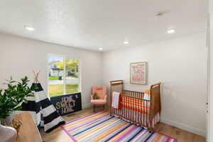 Bedroom featuring light wood-style flooring, a textured ceiling, a nursery area, and recessed lighting
