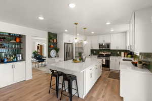 Kitchen with white cabinetry, stainless steel appliances, a center island, light stone counters, and hanging light fixtures