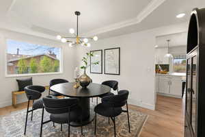 Dining area featuring a tray ceiling, ornamental molding, light wood-type flooring, and hanging lights