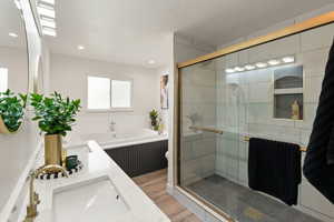 Full bath featuring double vanity, light wood-type flooring, a stall shower, a textured ceiling, and a garden tub