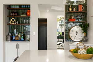 Bar area with open shelves, white cabinetry, and light stone countertops