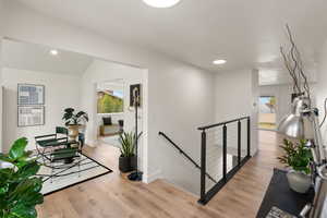 Hall featuring an upstairs landing, light wood-style flooring, recessed lighting, and vaulted ceiling