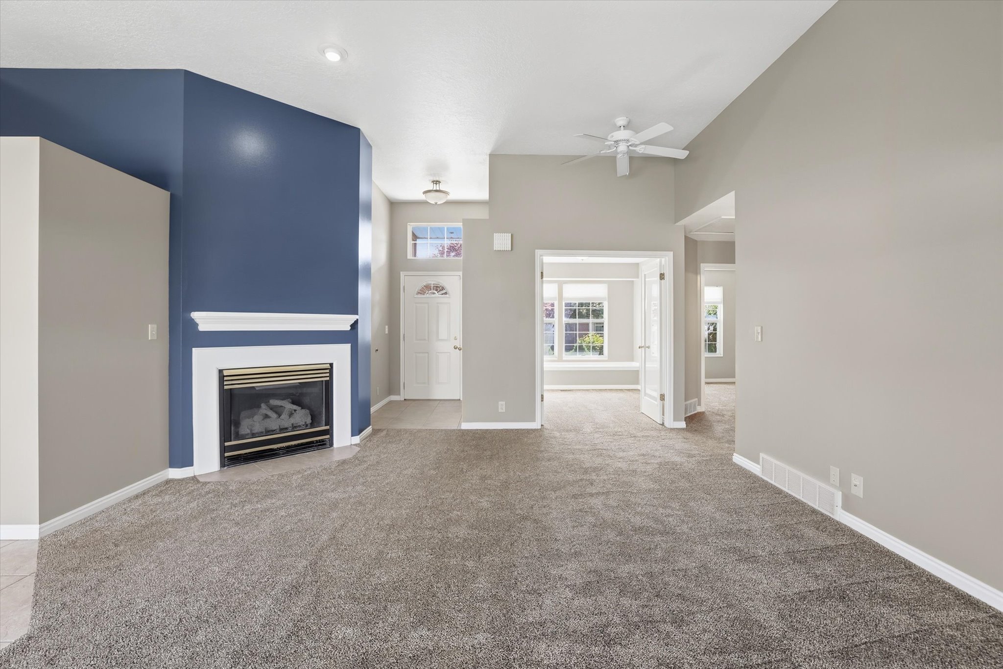 Living room with a ceiling fan, a fireplace with flush hearth, and a high ceiling